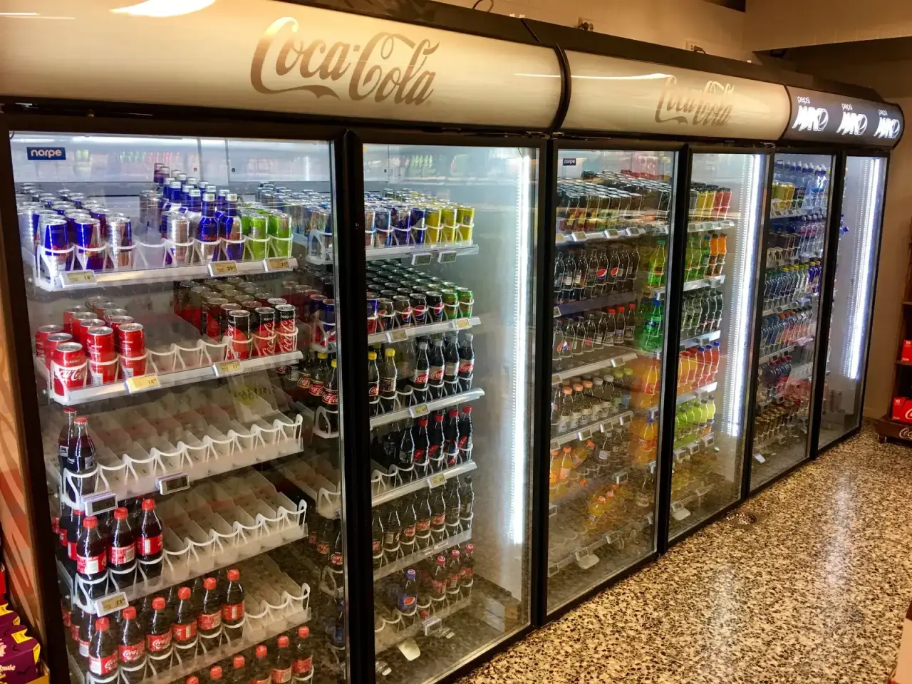 Glass-door merchandiser coolers stocked with bottled and canned drinks in a store — commercial refrigeration repair